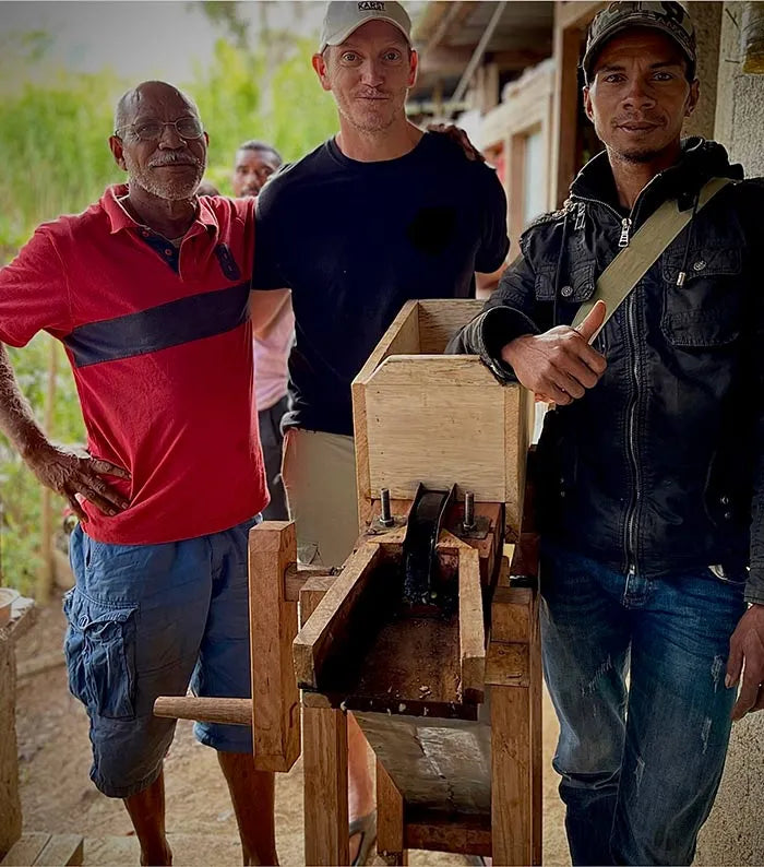 Three men standing around a wooden machine in an outdoor setting